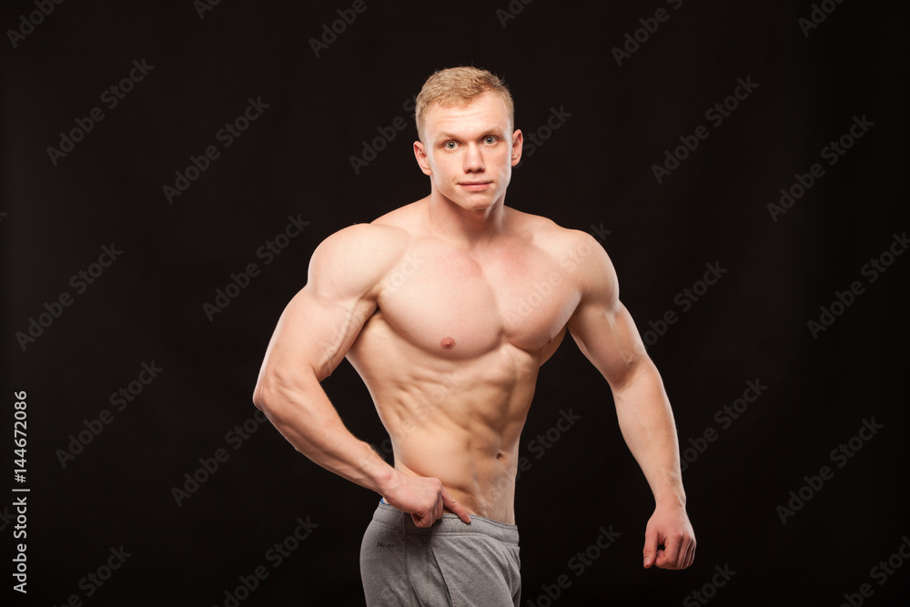 Athletic handsome man fitness-model is showing six pack abs and oblique abdominal muscles. isolated on black background with copyspace Athletic handsome man fitness-model is showing six pack abs and oblique abdominal muscles. isolated on black background with copyspace