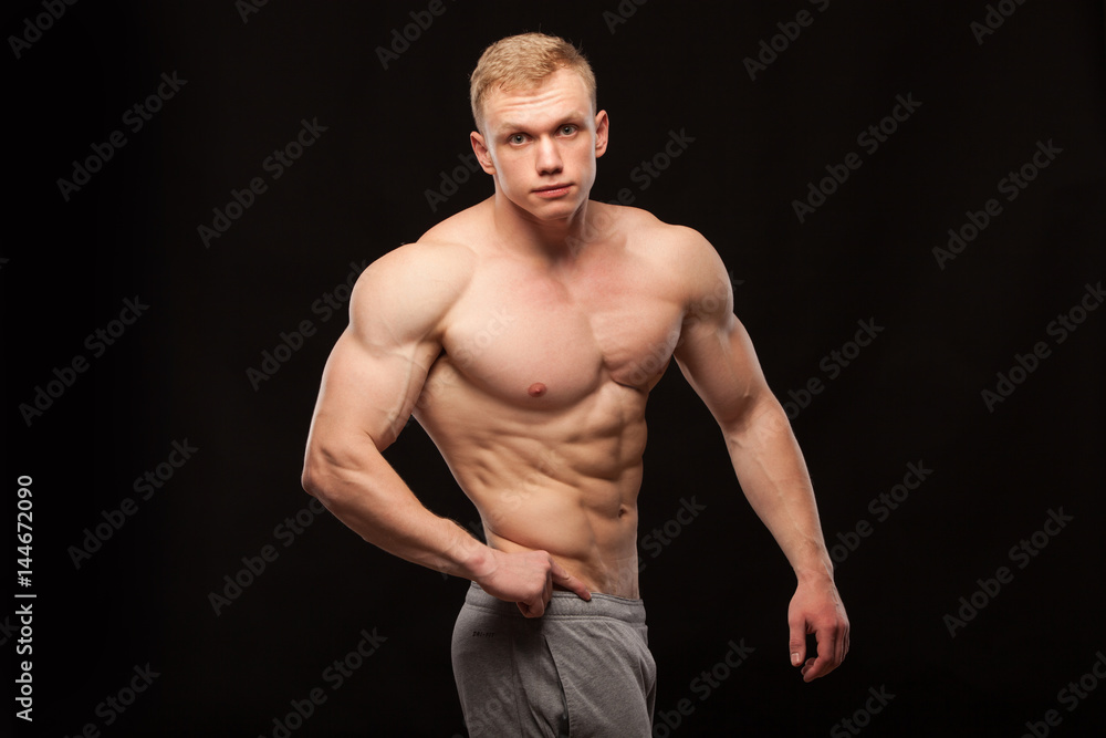 Athletic handsome man fitness-model is showing six pack abs and oblique abdominal muscles. isolated on black background with copyspace