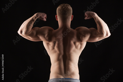 Athletic handsome man fitness-model turned back showing his perfect body. isolated on black background with copyspace