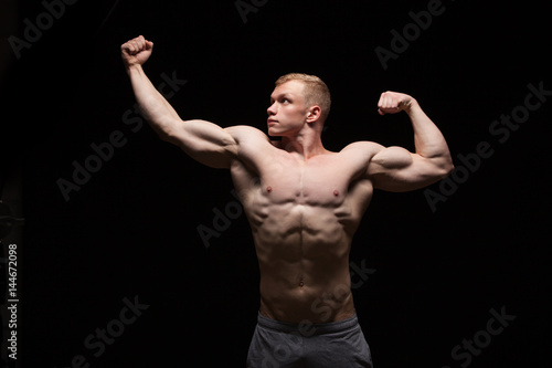 Athletic handsome man fitness-model is showing six pack abs and looking on the left. isolated on black background with copyspace