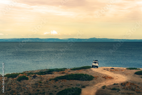 Off-road vehicle on a gravel road in front of the sea at sunset