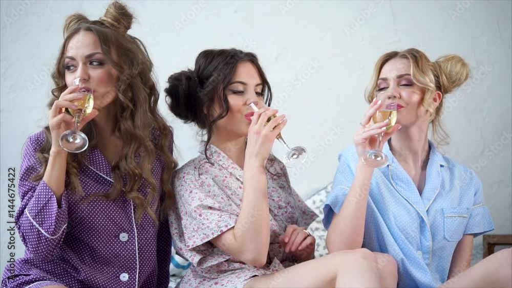 Concept of hen-party. Three pretty girlfriends drinking champagne wine together on a pajama party. Women chatting and laughing. Concept of hen-party. Three pretty girlfriends drinking champagne wine together on a pajama party. Women chatting and laughing.
