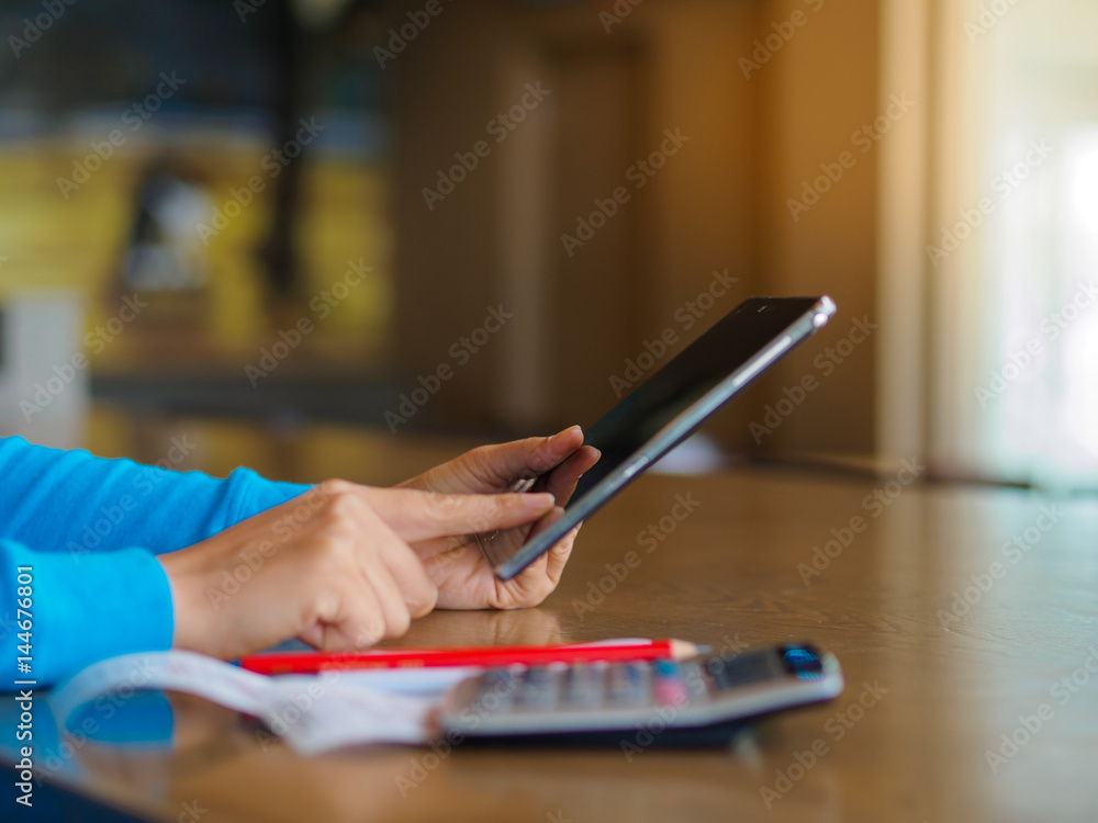 Fototapeta premium Pretty Young womans hands holding and using tablet for online shopping, bill, pencil and calculator on the table. Online payment. Female working on tablet in a cafe.