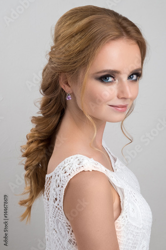 Portrait of a blonde with evening make-up and gathered in a braid hair in a white lace top.