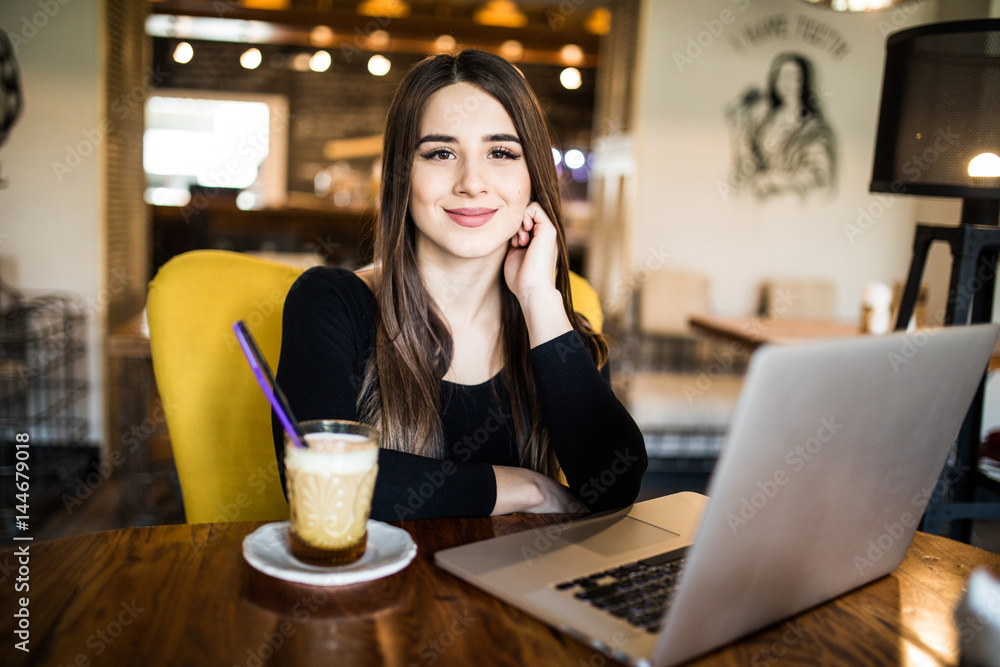 Pretty brunette using her laptop in a coffee shop and look at camera Pretty brunette using her laptop in a coffee shop and look at camera