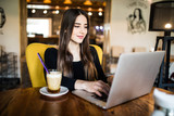 Indoor portrait of a young girl she works as a freelancer in a cafe drinking a delicious hot Cup of coffee from text send mail loads the photo instagram freelancer