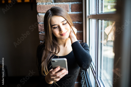 Woman sitting by a window, looking at her cell phone photo