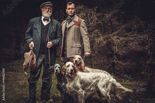 Fotografie, Obraz Two hunters with dogs and shotguns in a traditional shooting clothing