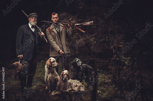 Fotografia, Obraz Two hunters with dogs and shotguns in a traditional shooting clothing