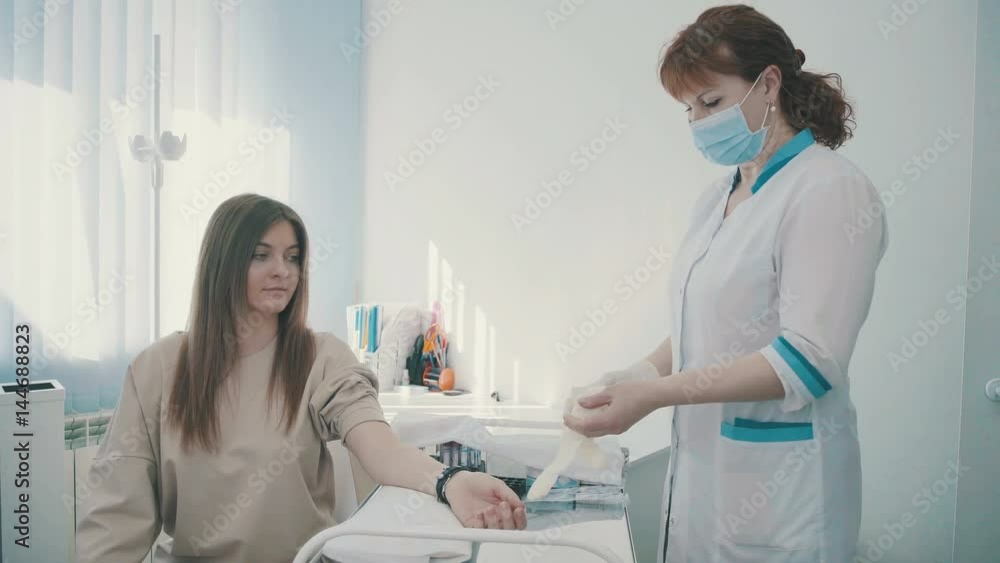 A young woman patient gives blood from a vein. A doctor or nurse prepares the patient for taking tests (blood from the vein). Bandage and gauze on an arm after a blood test or shot. A young woman patient gives blood from a vein. A doctor or nurse prepares the patient for taking tests (blood from the vein). Bandage and gauze on an arm after a blood test or shot.