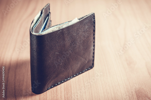 Black wallet with money on wooden table.