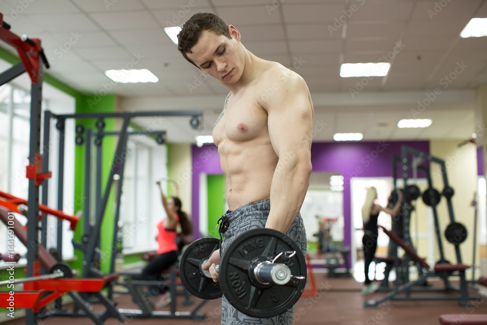 Naklejka premium Muscular man working out in gym doing exercises with barbell, strong male naked torso abs