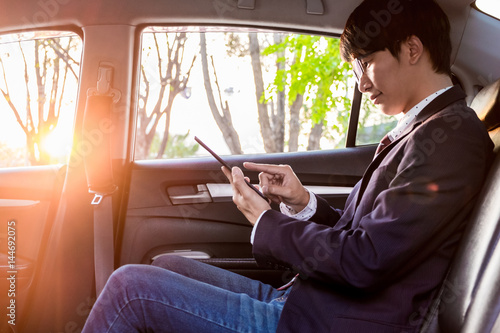 young handsome businessman working in back of car and using a tablet or smart phone