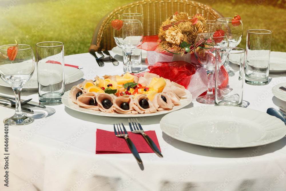 Fototapeta premium Sunlit cold plate with cheese and ham and fruit. Decorated table in the garden