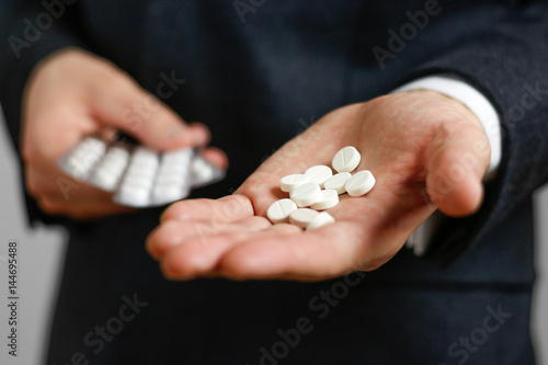 Businessman holds in hands a lot of white pills and packs of tablets