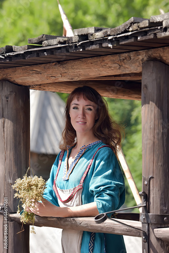 Viking woman, brunette in a blue linen dress, on the walls of the wooden old house. photo