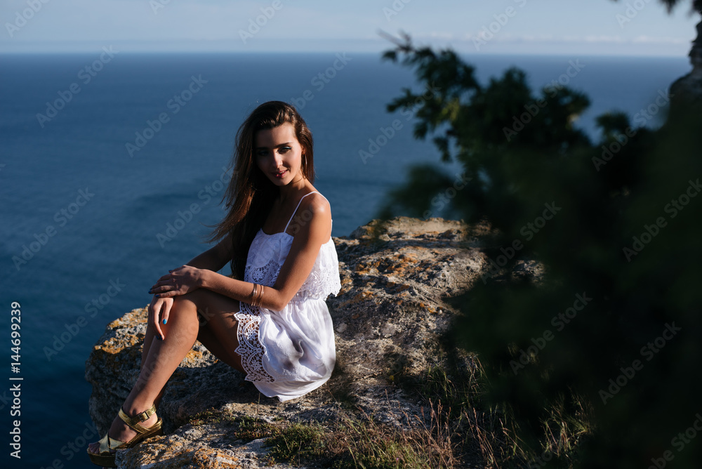 Portrait of attractive brunette girl on the stone. She wears white dress. Portrait of attractive brunette girl on the stone. She wears white dress.