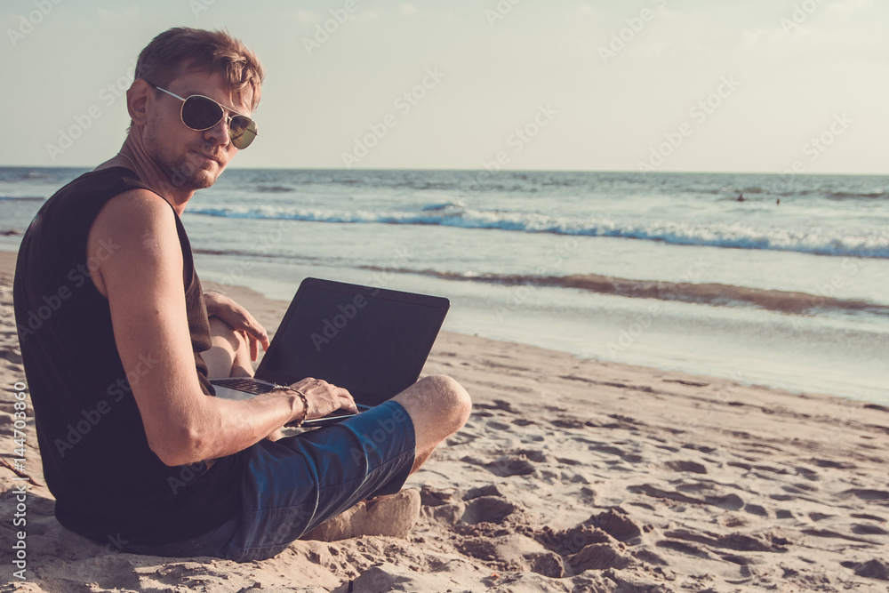 Young man are working on laptop computer on the beach. Downshifting and freelance concept.