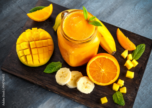 Fresh Orange smoothie drink with banana, mango, carrots on black wooden board.
