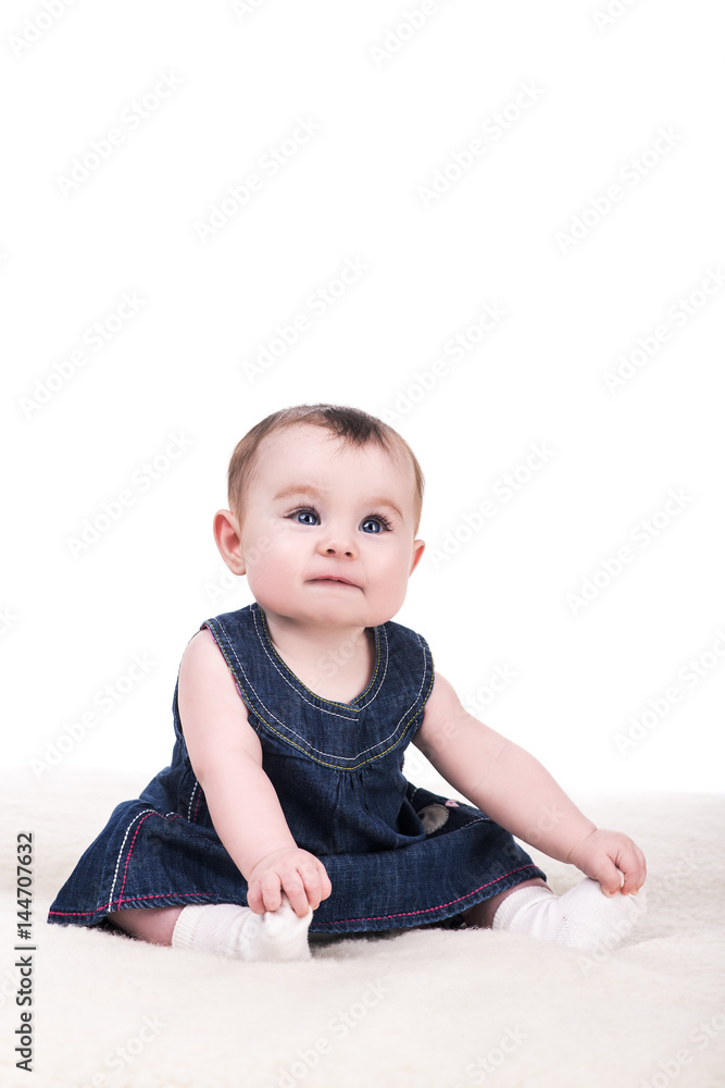cute baby girl with big blue eyes and long eyelashes, isolated on white. adorable child girl sitting on soft blanket in blue dress