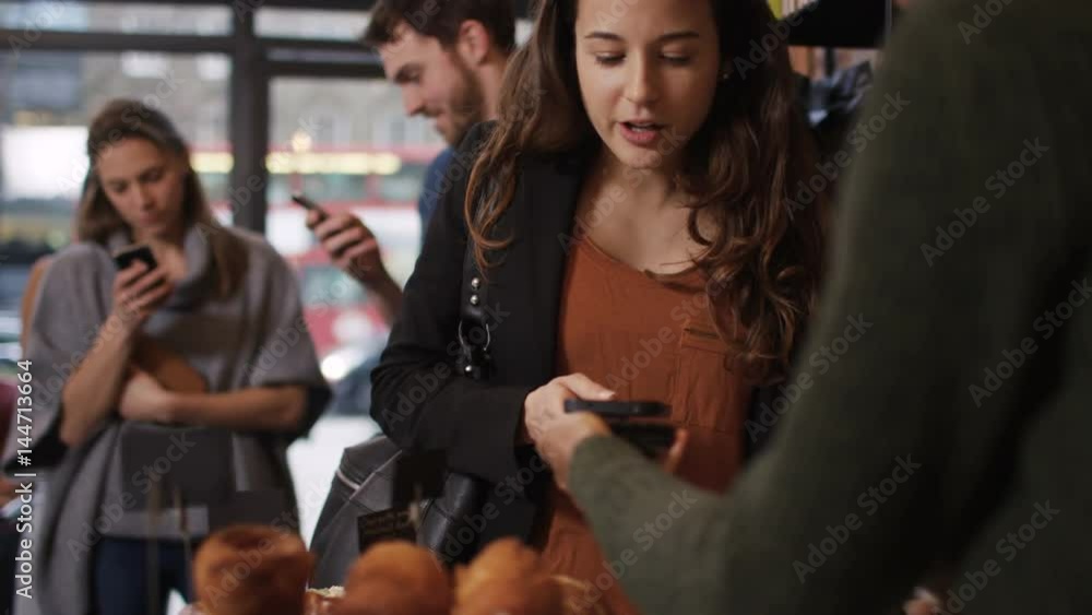 Customer in cafe makes payment with smartphone while queue of customers wait Customer in cafe makes payment with smartphone while queue of customers wait