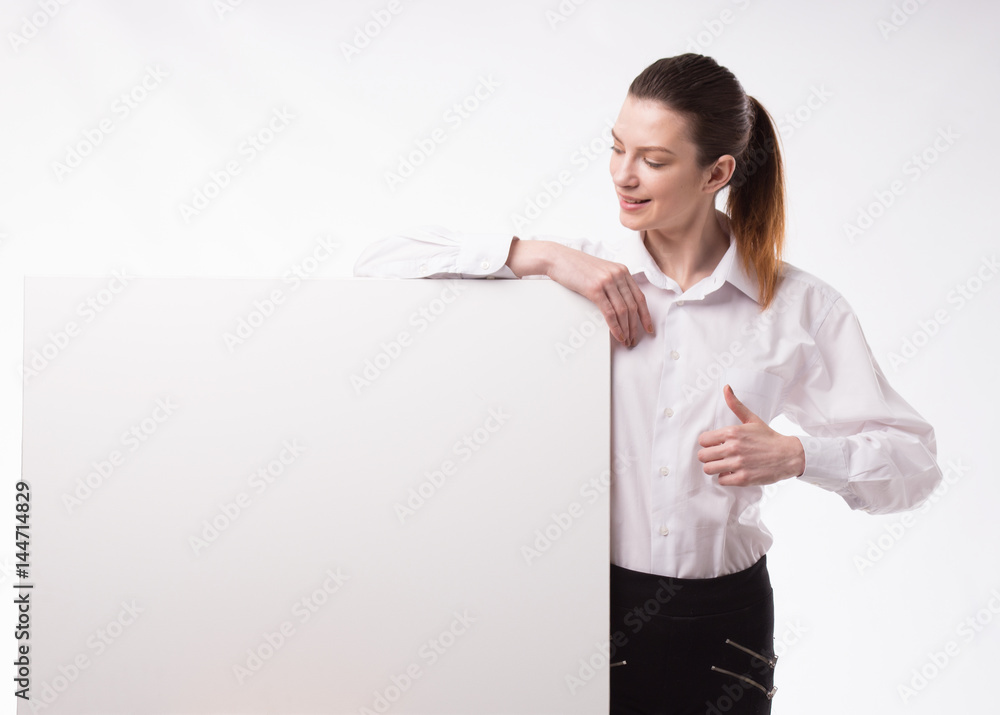 Young happy woman showing presentation, pointing on placard over gray background Young happy woman showing presentation, pointing on placard over gray background