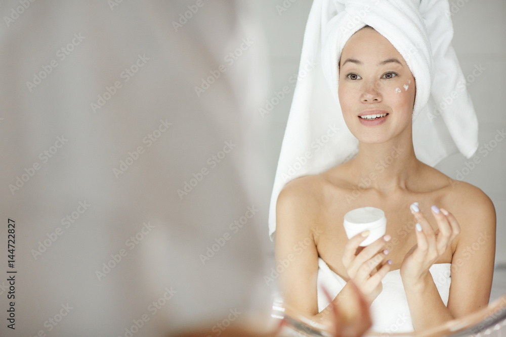 Girl applying facial cream in front of mirror Girl applying facial cream in front of mirror