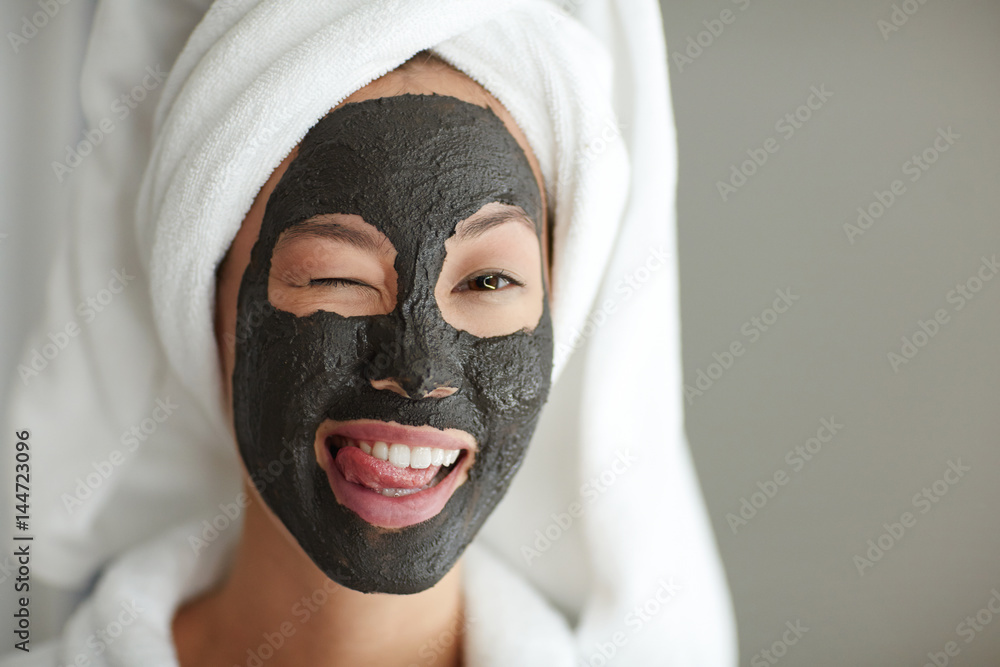Flirty girl winking while having purifying mask Flirty girl winking while having purifying mask
