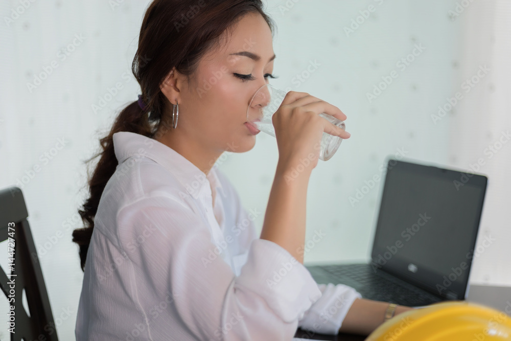 Asian business woman and engineering in dress sitting by the table in office and drinking water Asian business woman and engineering in dress sitting by the table in office and drinking water