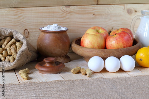 Composition of various products. Flour, nuts, milk, apples, eggs and lemon are on wooden background.