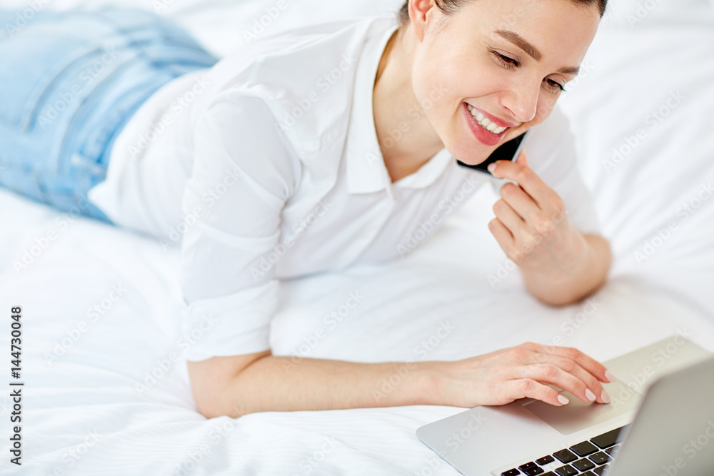 Happy girl speaking on smartphone and browsing in the net while lying on bed