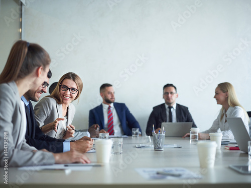 Group of cheerful business people smiling and chatting at meeting table in conference room photo