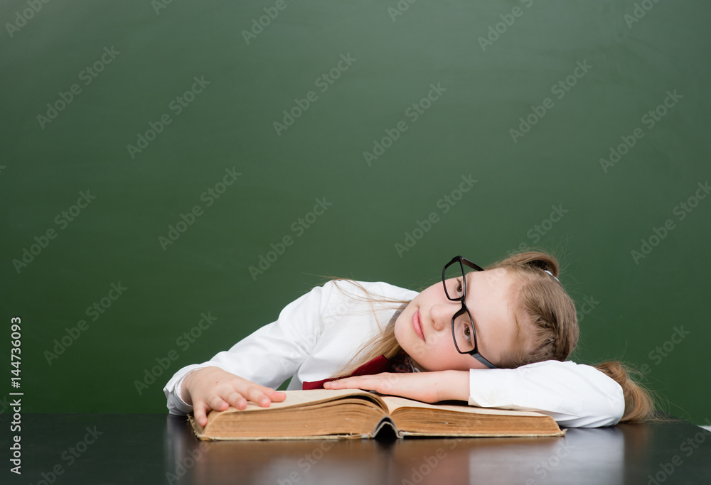 Happy teen girl lying on a big book near empty green chalkboard and looking up