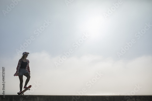 Silhouette of a young woman standing with skateboard © cristovao31