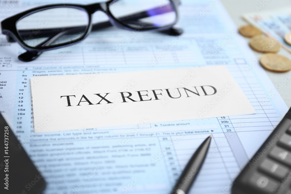 Paper sheet with text TAX REFUND and documents on table Paper sheet with text TAX REFUND and documents on table