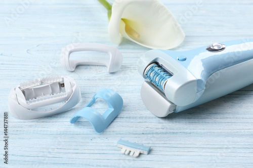 Modern epilator with accessories on wooden background