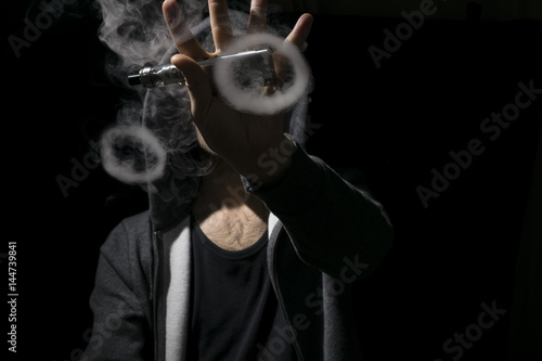 Young man holding electronic cigarette and doing vaping tricks.