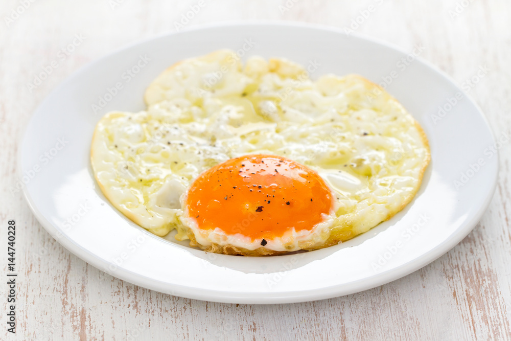 fried egg on white plate on wooden background