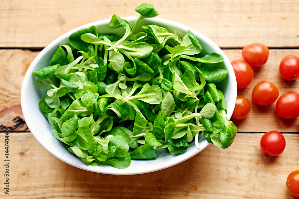Cherry tomatoes and basil salad in a white cup on a wooden table. Cherry tomatoes and basil salad in a white cup on a wooden table.