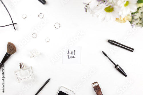 A bouquet of flowers with Just love written in calligraphic style on paper on flowers on a white background with female things. Flat lay, top view