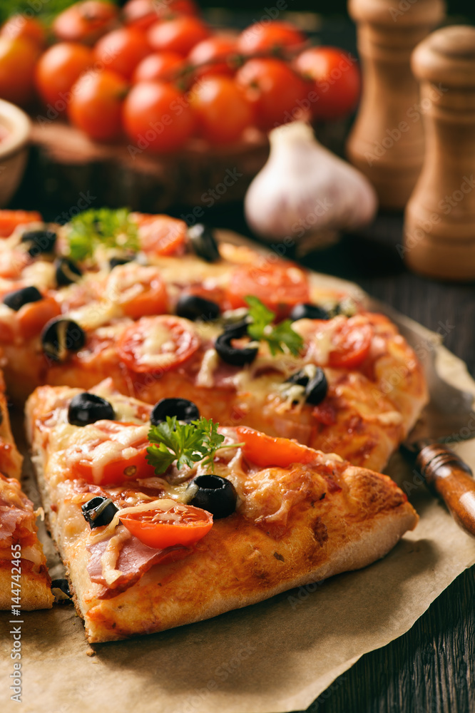 Homemade pizza with ham, cheese, tomatoes and olives.