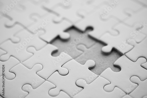 white jigsaw/puzzle whit one gap, over black wooden table background, symbol of problem solving