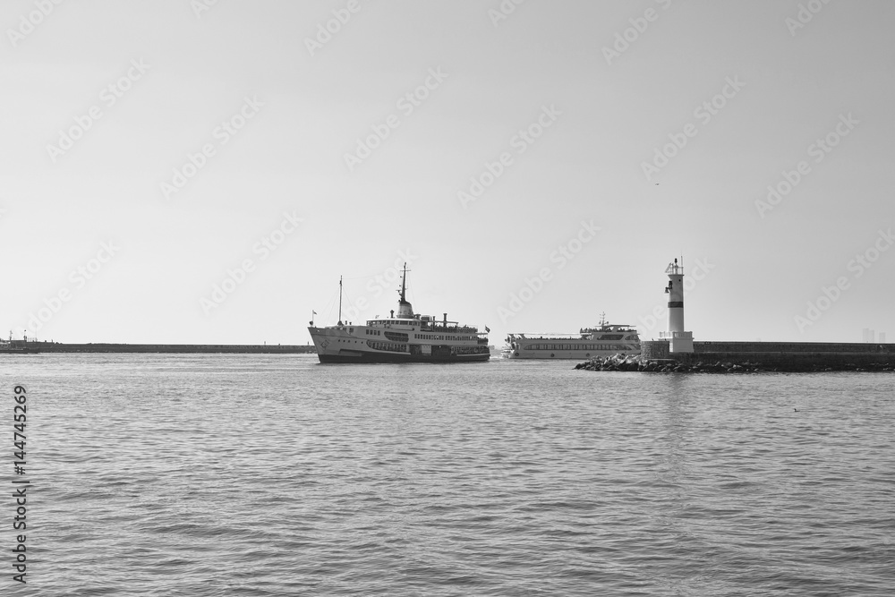 Black and white photography of traditional public ferry arriving to Kadikoy station. Water breaker and a motorboat are also in the view.