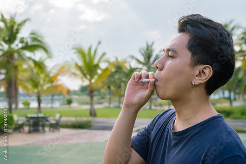casual young man and smoking a cigarette in his mouth. Man smoking a cigarette on park outdoor.