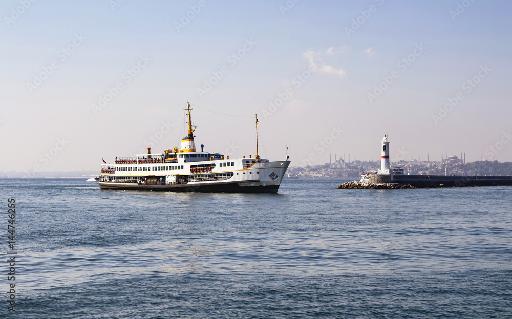 Traditional public ferry arriving to Kadikoy station in Istanbul. Water breaker is also in the view. Hagia Sophia and Blue Mosque are in the background.