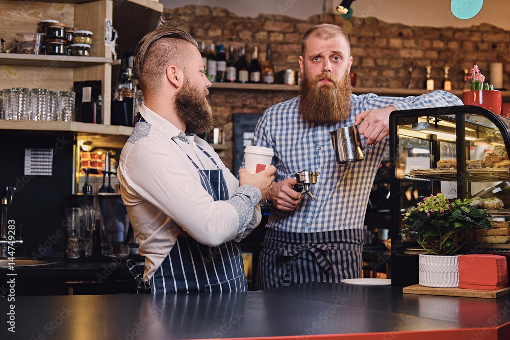 Two bearded hipster coffee shop owners at the counter.