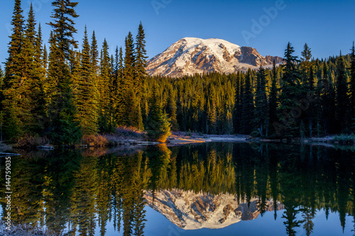 Mountain reflected in lake with trees at sunrise