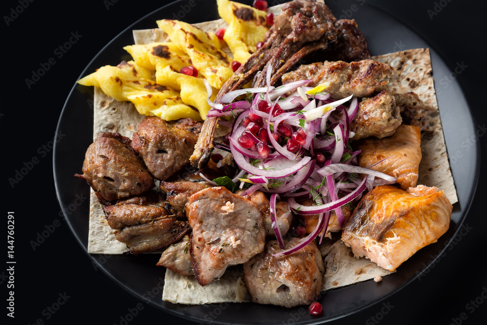 Lyulya kebab, shish kebab, grilled salmon fish, onion and pomegranate grains on black plate. Close up image with selective focus