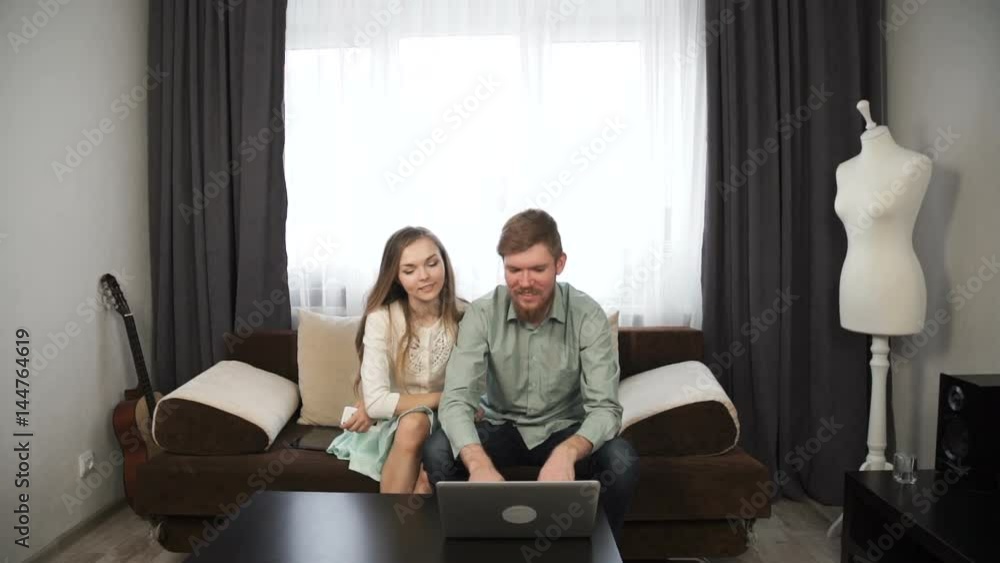 Couple is sitting on the couch sofa at home Look at the laptop screen and smile Couple is sitting on the couch sofa at home Look at the laptop screen and smile