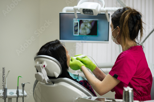 Dentist at work examining woman's teeth in dental clinic with remote camera. Picture of teeth is on the screen. dental technologies.